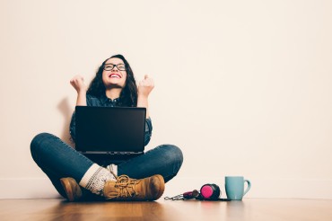 Girl sitting on the floor with a laptop raising his arms with a look of success