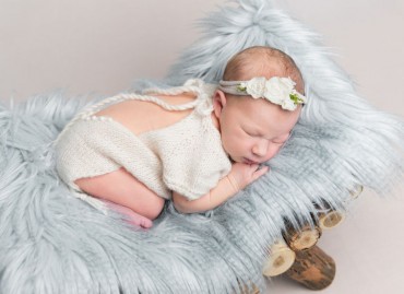 Sweet newborn baby girl with headband sleeps on small wooden crib.