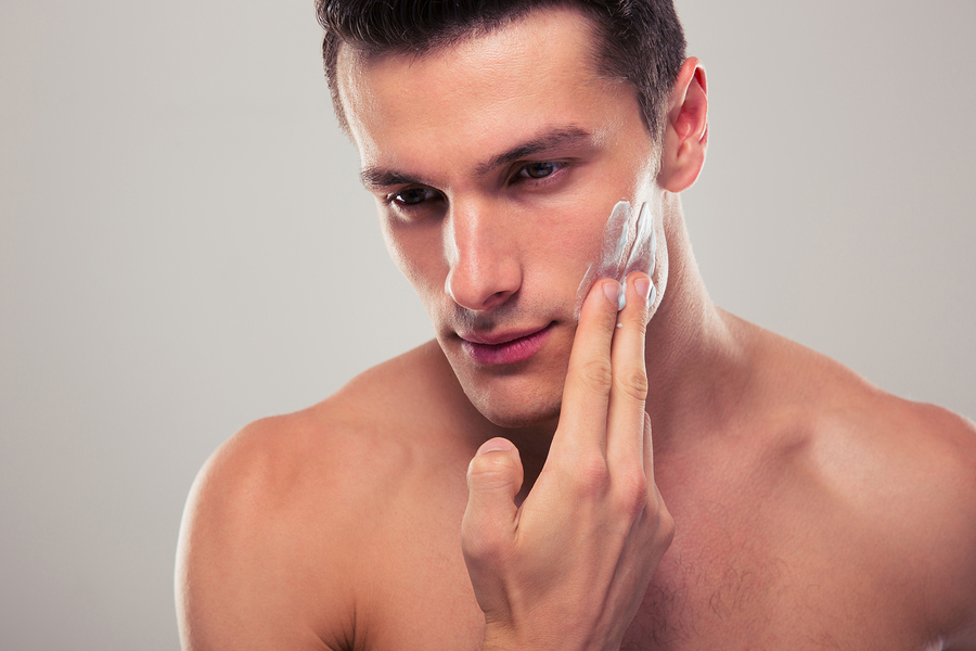 Handsome man applying facial cream over gray background